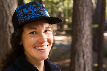 Young caucasian woman dressed in outdoors clothing stands in a forest and smiles at viewer