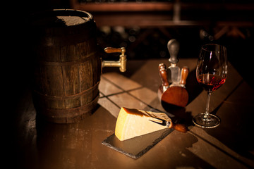Small barrel with wine, cheese, wine glass and accessories placed on a wooden table in a wine vault.