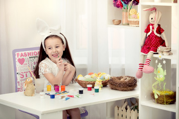 Happy easter! A beautiful child girl painting Easter eggs. Happy family preparing for Easter. Cute little child girl wearing bunny ears on Easter day.