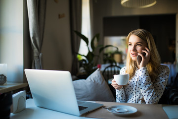 Blonde young businesswoman using her phone and laptop at a cafe