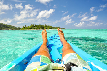 Stunning view of a young man's legs in a kayak near Motu Koromiri, a small island in the lagoon of Rarotonga near Muri Beach. Cook Islands in the South Pacific Ocean, Clear, shallow water, palm trees.