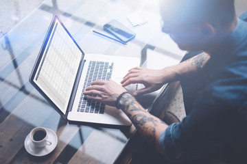 Adult tattooed coworker using laptop while working at sunny office.Finance reports on notebook screen.Blurred background.Horizontal.