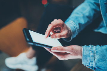 Closeup view of female hands holding modern smartphone and touching white blank screen.Horizontal, blurred background, bokeh effects.