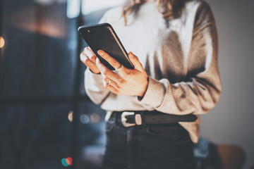Young hipster girl holding modern smartphone in hands and touching screen.Horizontal, blurred background, bokeh effects.