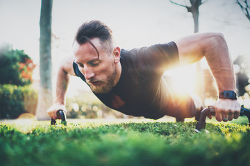 Fitness lifestyle concept.Muscular athlete exercising push up outside in sunny park. Fit shirtless male fitness model in crossfit exercise outdoors.Sport fitness man doing push-ups.Blurred background.