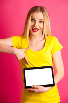 Beautiful blonde teenage woman pounting in blank tablet as advertisement over pink background