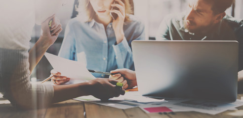 Fototapeta premium Group of young coworkers working together in modern coworking studio.Woman using smartphone for talking with partners about new startup project.Teamwork concept.Wide.