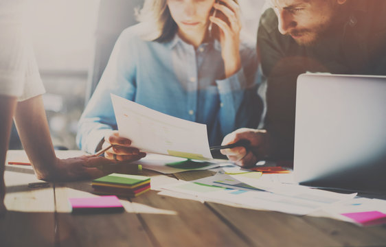 Group of young coworkers working together in modern coworking studio.Woman using smartphone for talking with partners about new startup project.Teamwork concept.Blurred background.