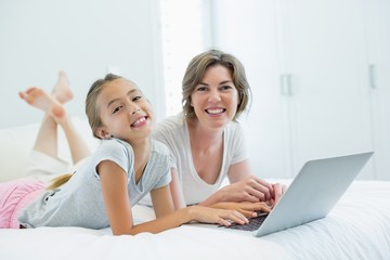 Fototapeta na wymiar Smiling mother and daughter using laptop on bed