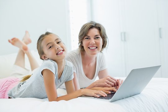 Smiling mother and daughter using laptop on bed