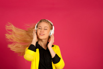 Beautiful young woman in black and yellow vibrant dress dances as she listens to the music over pink background