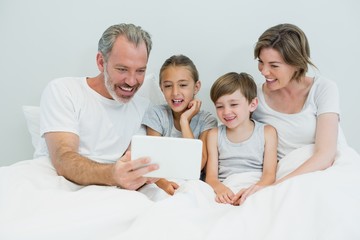 Family using digital tablet on bed in bedroom at home