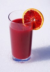A glass of fresh ruby red blood orange juice with a blood orange slice in winter in the snow