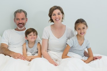 Obraz premium Happy family sitting together on bed in bedroom at home