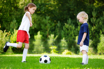 Two cute little sisters having fun playing a soccer game on sunny summer day. Sport activities for children.