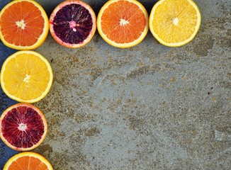 Oranges, blood oranges, and cara cara oranges cut in half forming a border frame on a stone...