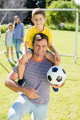 father with football carrying his son on shoulder