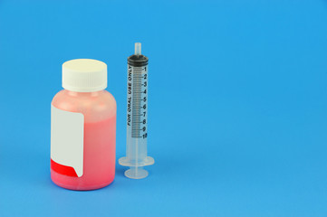 Prescription medicine bottle and oral syringe for baby isolated on blue background