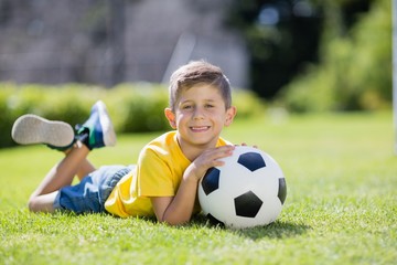 Naklejka premium Boy lying on grass with football in the park