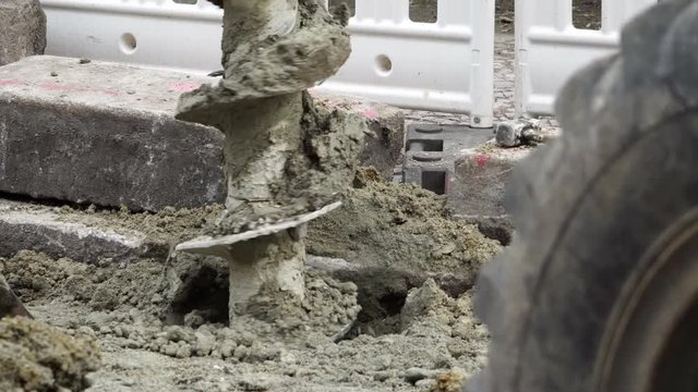 Handheld closeup shot of a post-hole earth drill auger drilling machine making a hole in the ground on a construction site.
