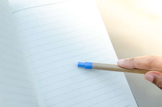 Finger with pen pointing to notebook on nature light background
