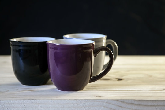 Purple, black and gray mugs on plain wooden table.