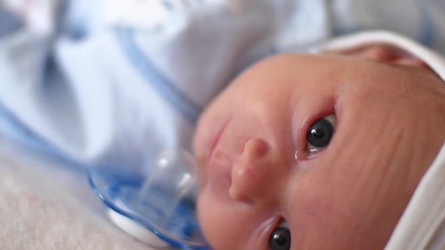 A cute little baby is looking into the camera and is happy on a white bed sheet. The baby looks around