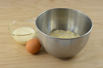 Ingredients for cornbread batter with mix in mixing bowl, egg and milk in measuring cup