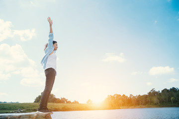 Happy woman with hands up standing on rock and lagoon at sunset