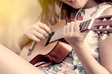 Young asian woman playing acoustic guitalele in the park in vintage color tone