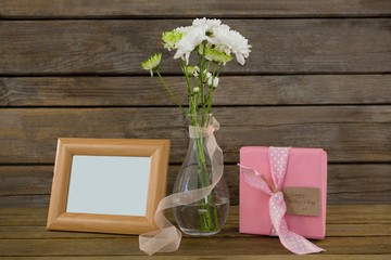 Gift box, photo frame and flower vase on wooden surface