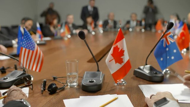 Canadian leader at international summit. Flag of Canada, white paper, pencil and microphone. Political delegates from different countries of G20 applaud the speaker. High-level discussion of policy