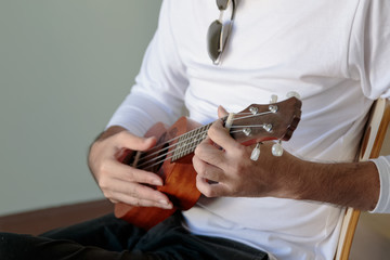 Fototapeta premium Closeup handsome man was playing a Ukulele enjoyed in the room