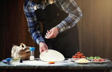 man in an apron preparing a pizza, knead the dough and puts ingredients