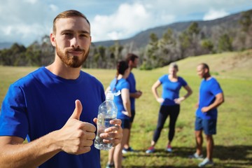 Fototapeta premium Fit man showing thumbs up while holding water bottle