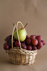  green pears and a large red grapes in a wicker basket On a brown paper background