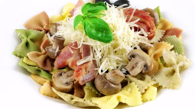 Close-up view of colored bowtie pasta with parmesan cheese, mushrooms, beacon and basil leaf
