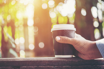 Man hand holding paper cup of coffee on natural morning background.