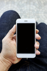 mockup image of hands holding white mobile phone with blank black screen, soft-focus in the background. over light and film colors tone