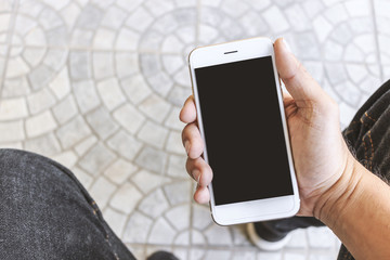 mockup image of hands holding white mobile phone with blank black screen, soft-focus in the background. over light and film colors tone