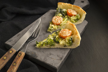 pie with broccoli, cherry tomatoes and cheese on black background