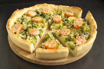 pie with broccoli, cherry tomatoes and cheese on black background