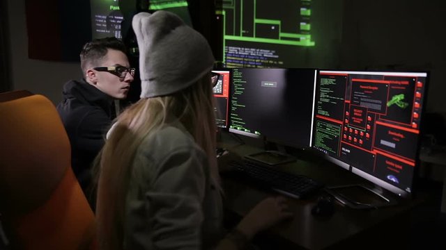 Two hackers at the computers. Computers screens with code on a background. HD.