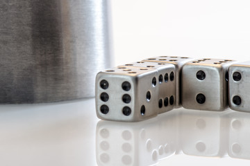 Würfel und Würfelbecher auf weißer Glasplatte mit Spiegelung - Würfelspiel / Spielwürfel /...