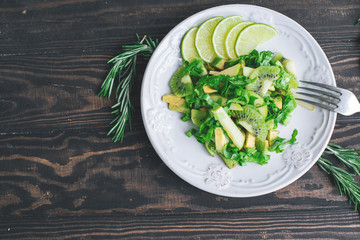Healthy vegetarian food salad ingredients avocado, apples, kiwi, salad decorated with lime and rosemary on the wooden table top view