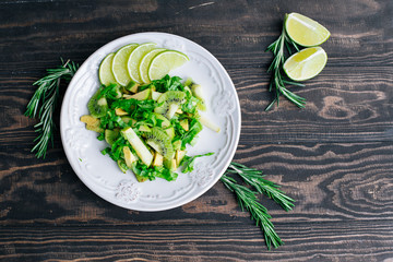 Healthy vegetarian food salad ingredients avocado, apples, kiwi, salad decorated with lime and rosemary on the wooden table top view
