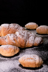 Croissant big and small with chocolate and powdered sugar on black background. French dessert