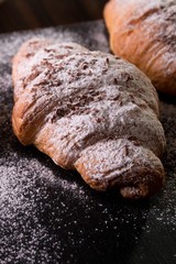 Croissant big and small with chocolate and powdered sugar on black background. French dessert