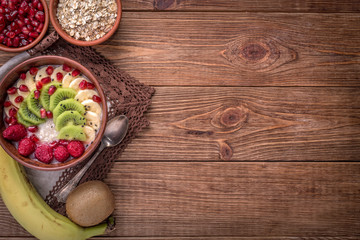 Oatmeal porridge with banana, kiwi fruit , raspberries and garnet for healthy breakfast on rustic wooden background. 