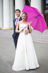 Young couple hugs in wedding gown with pink umbrella